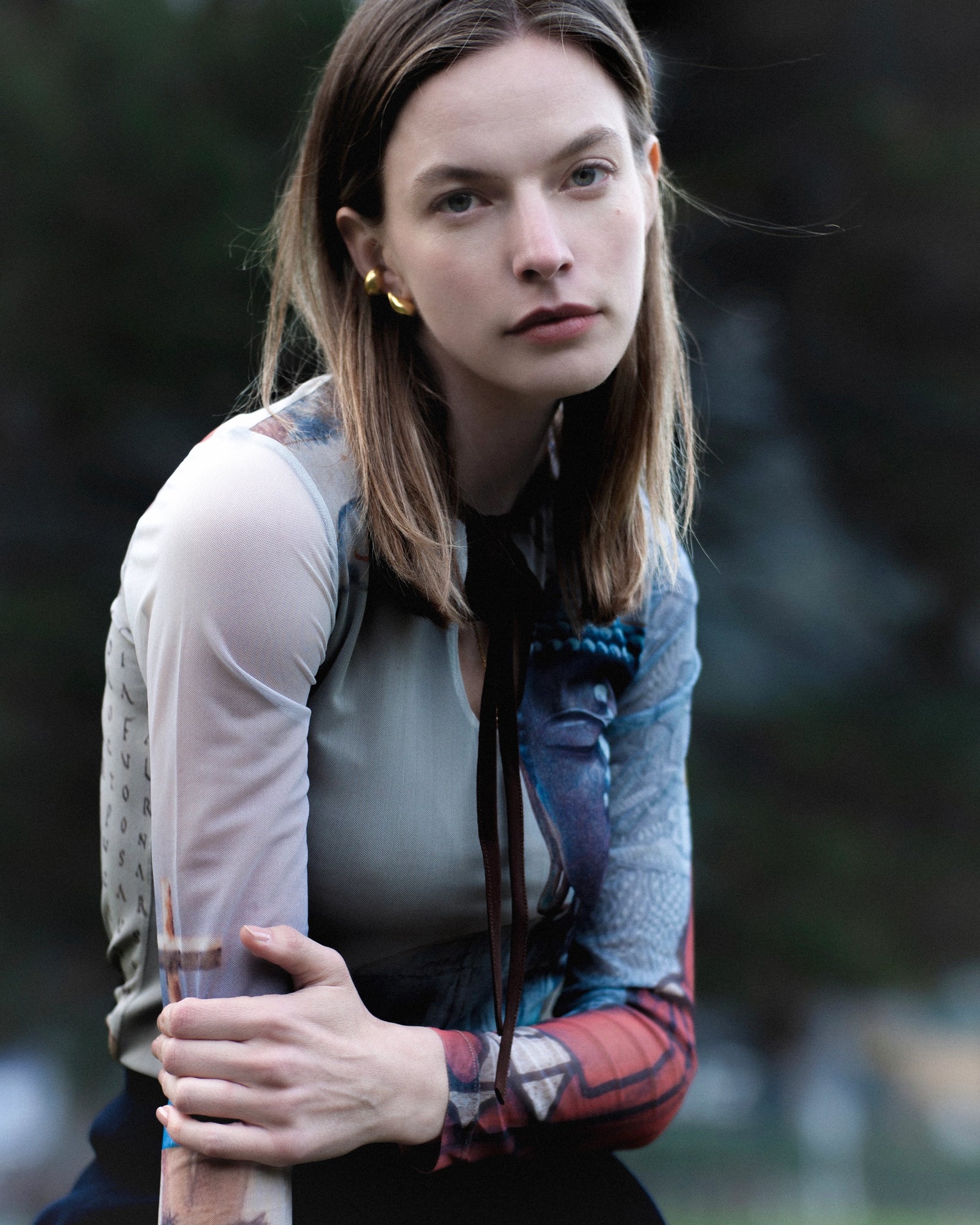 Shopigo markasına ait doğada çekilmiş portre; transparan Buddha baskılı uzun kollu üst ve sade altın küpelerle minimal ruh halini yansıtır. Pentome Studio’da çekilmiştir.
A natural outdoor portrait for the brand Shopigo, featuring a sheer Buddha-printed long-sleeve top and simple gold earrings that evoke a minimal, serene mood. Photographed at Pentome Studio.