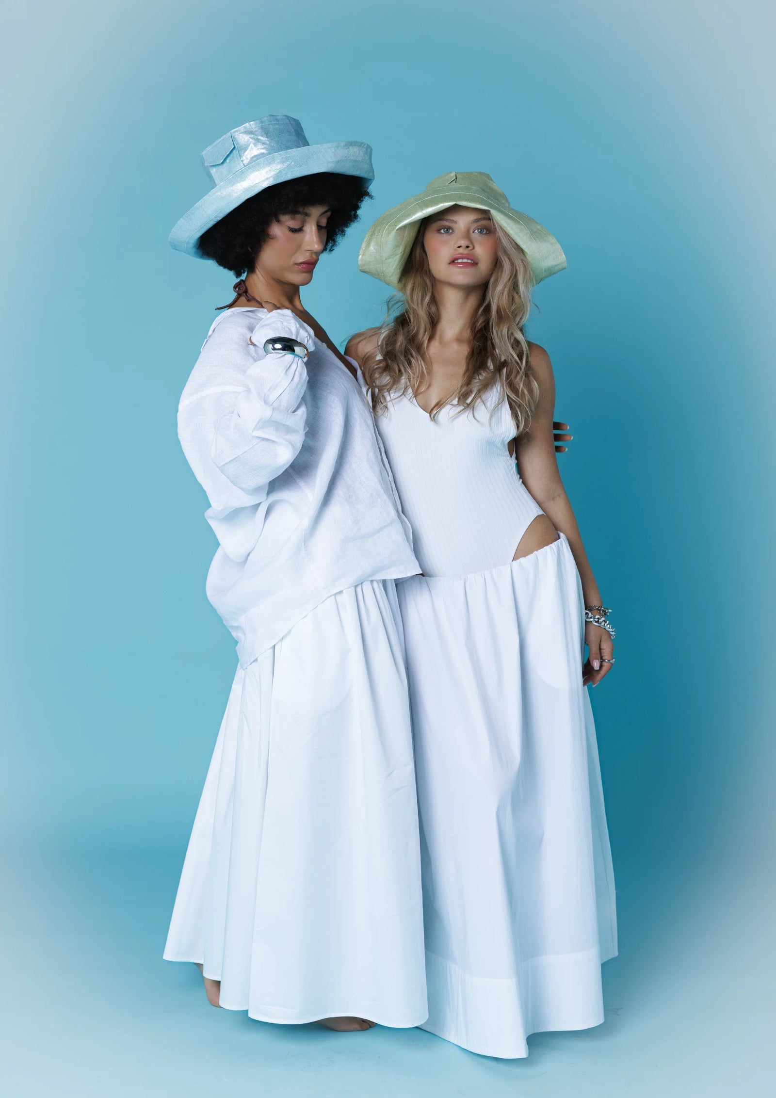 Pastel mavi ve yeşil şapkalarla zarif beyaz kıyafetli iki modelin uyumlu duruşu. Pentome Studio’da çekilmiştir.
Elegant harmony of two models in white outfits with pastel blue and green hats. Photographed at Pentome Studio.