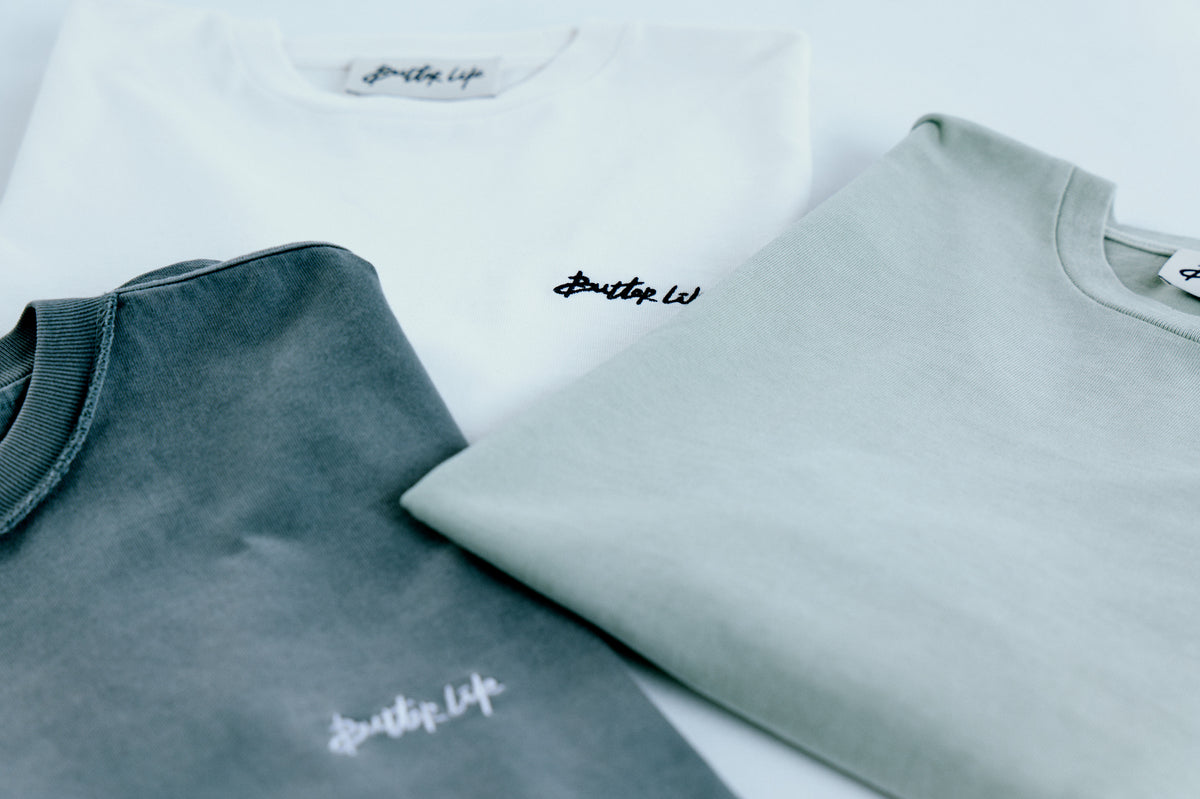 Üç tee’nin göğüs logolarına yakın plan; doku ve dikiş detayları. / Detail close-up of the three tees’ chest emblems; fabric and stitching highlighted.