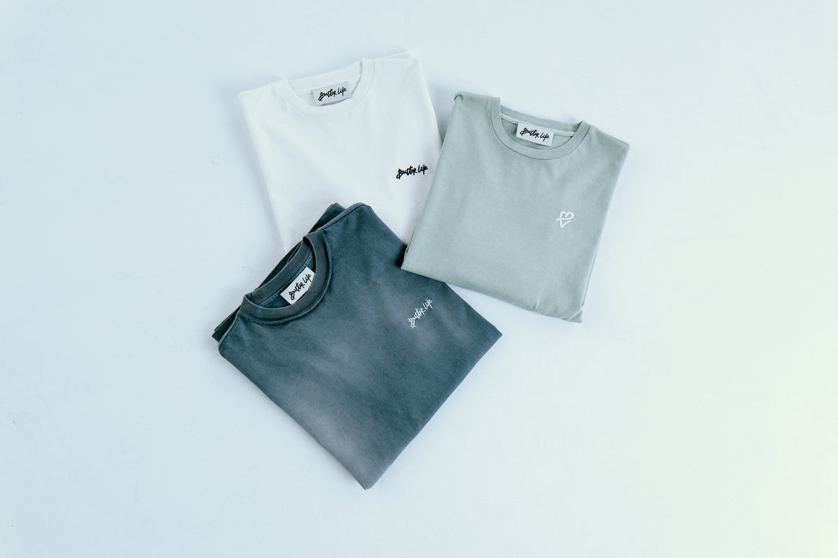 Üçlü katlı tee seti; yatay geniş kadraj, set temiz arka plan üzerinde. / Wide horizontal frame of folded tee trio on clean studio background.