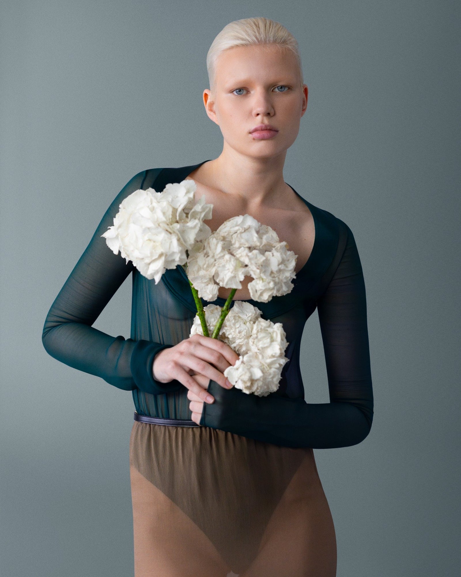 Beyaz ortancalarla yakın plan portre; şeffaf dokular ve çiçeklerin saf hacmi çağdaş romantizmi kuruyor. \ Close-up portrait with white hydrangeas; airy sheers and floral volume create contemporary romanticism.