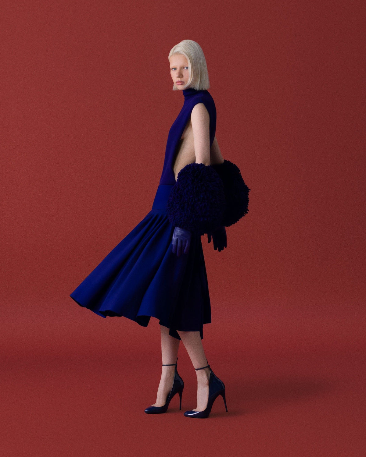 Kobalt mavisi hacimli etek ve el ısıtıcı detay; ince bilekten bağlamalı stilettolarla devinim yakalanıyor. \ Cobalt dress with a voluminous skirt and muff detail; movement captured with delicate ankle-strap stilettos.
